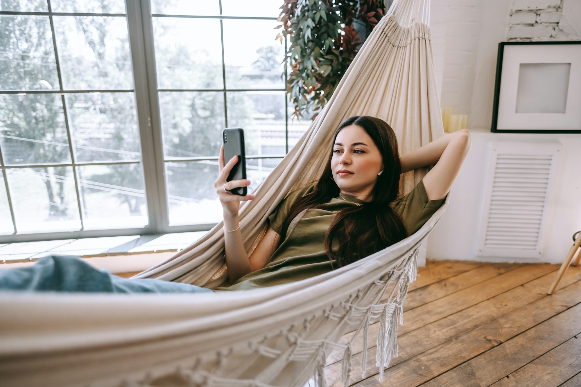 Attractive happy young woman relaxing in the home, lying in a hammock in living room